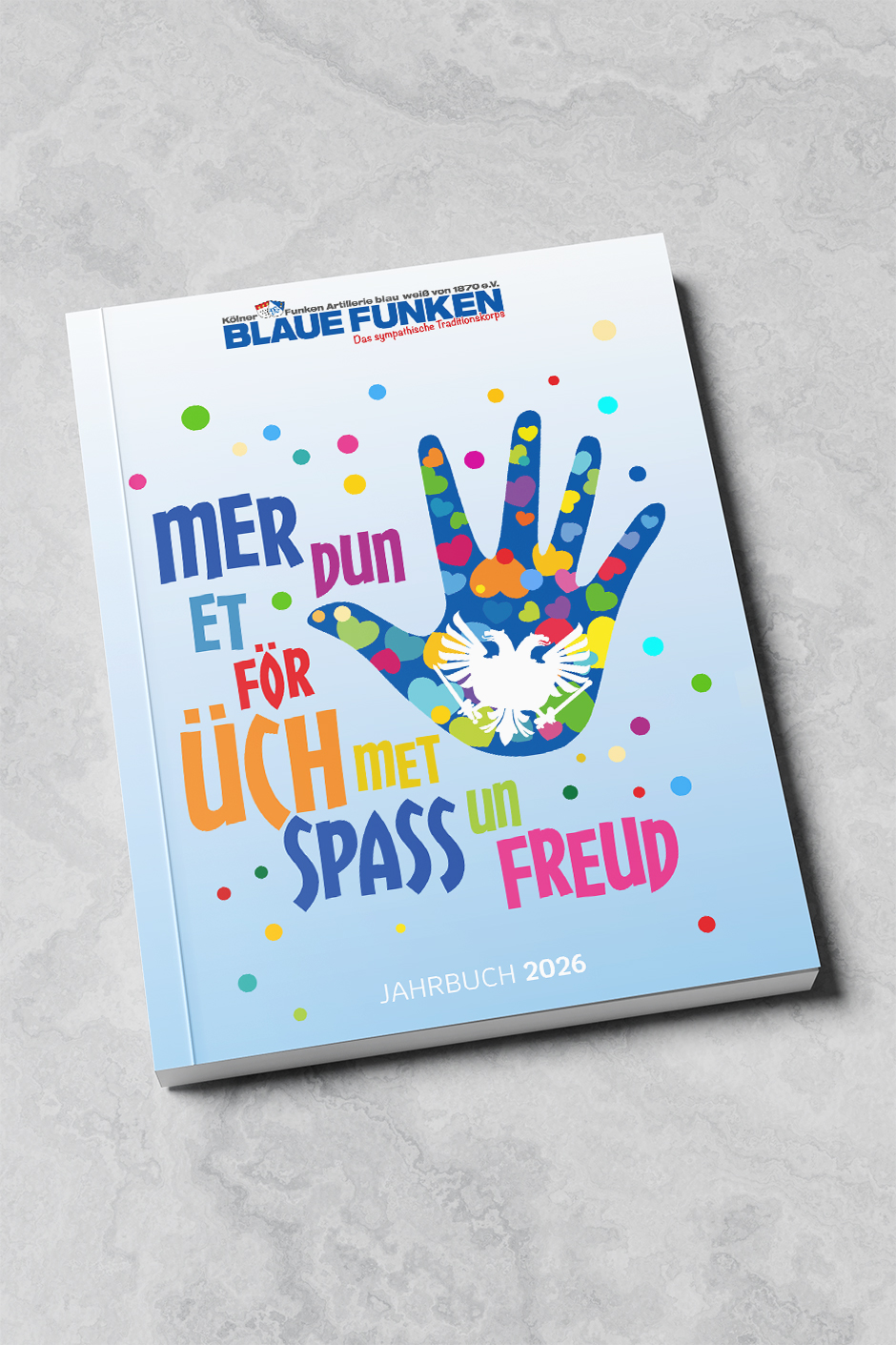 Jahrbuch 2026 der Blauen Funken mit buntem Cover, das eine Hand und den Text „Mer dun et för üch met Spass un Freud“ zeigt. Symbolisiert Freude und Gemeinschaft im Karneval.