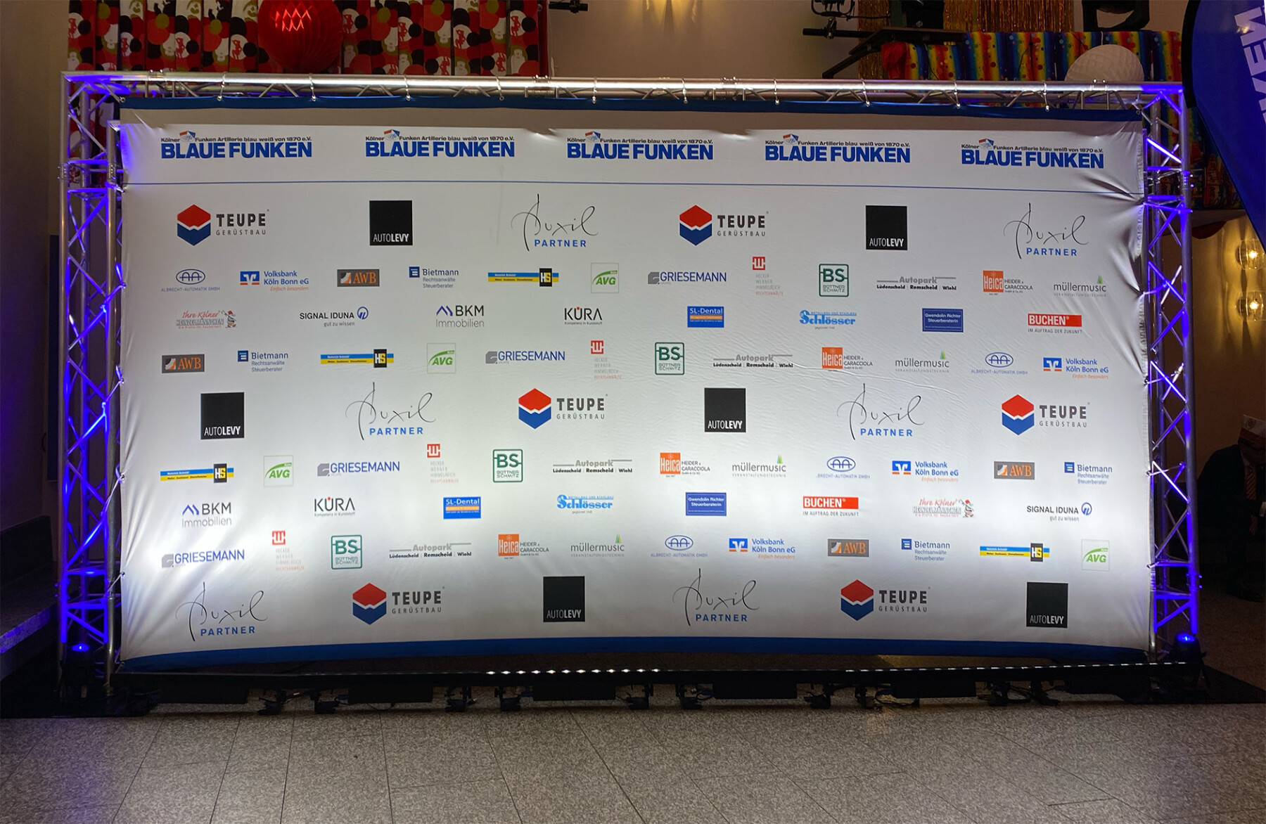 Banner mit Sponsorenlogos der Veranstaltung Blaue Funken, präsentiert auf einer Bühne. Die Logos sind gut sichtbar und repräsentieren verschiedene Unternehmen und Partner.