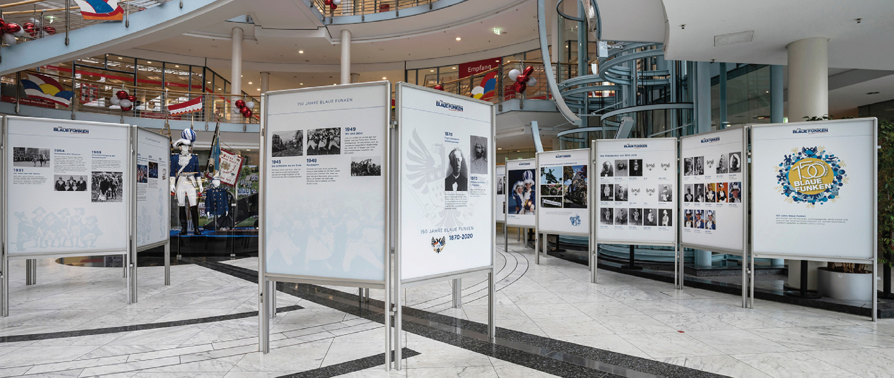 Ausstellung zum 150-jährigen Jubiläum der Blauen Funken mit historischen Informationen und Bildern, präsentiert in einem modernen Innenraum. Ideal für Besucher und Interessierte an Geschichte.