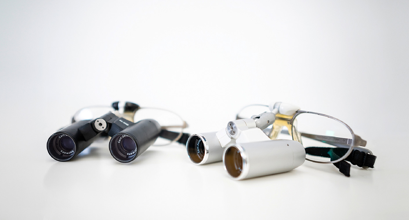 Zwei Paar zahnärztliche Lupenbrillen in Schwarz und Silber auf einem weißen Hintergrund, ideal für präzise Arbeiten in der Zahnmedizin und anderen feinen Handwerken.