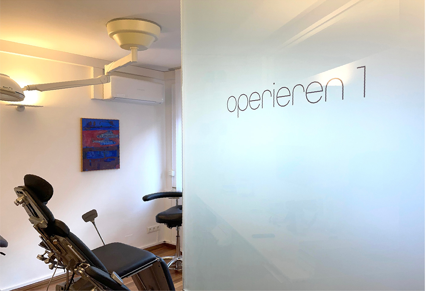 Moderne Arztpraxis mit einem Behandlungsraum. Sichtbare Behandlungsliege und Wand mit dem Schriftzug "operieren". Helle, freundliche Atmosphäre und Kunstwerk an der Wand.