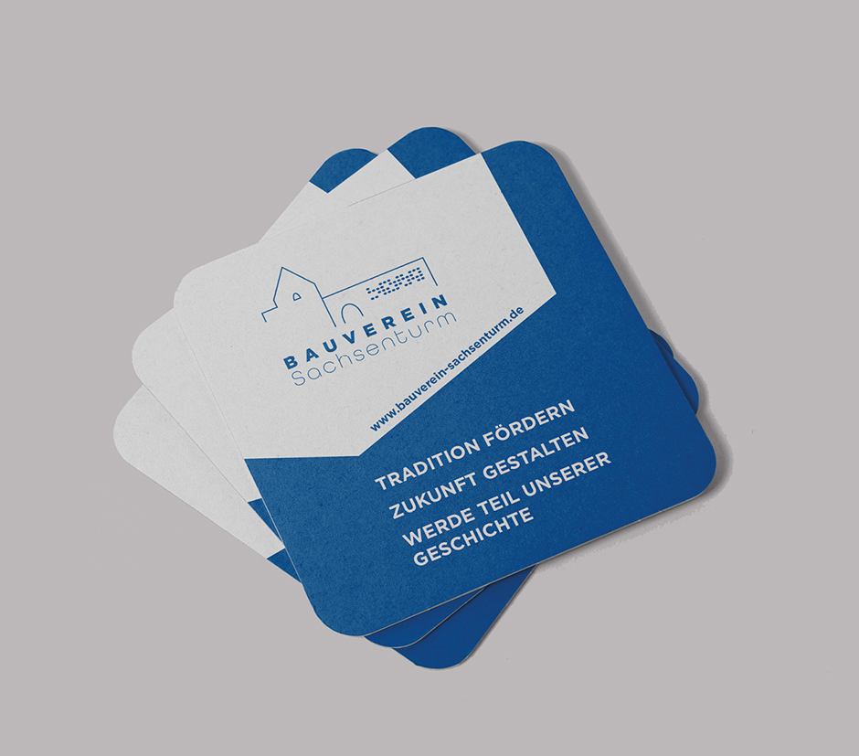 Bauverein Sachsensturm: Visitenkarten mit dem Slogan "Tradition fördern, Zukunft gestalten, werde Teil unserer Geschichte" in blau-weißer Gestaltung. Webseite im Hintergrund.