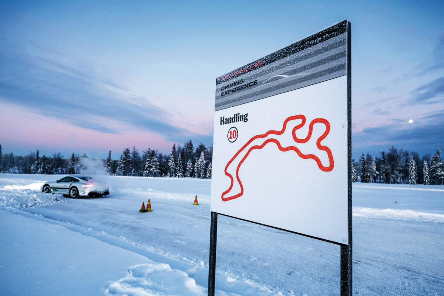 Schneebedeckte Rennstrecke mit einem Fahrzeug, das das Handling trainiert. Im Hintergrund ist ein Schild mit Streckenlayout und dem Hinweis "Handling 10" zu sehen.