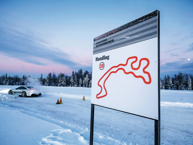 Schneebedeckte Rennstrecke mit einem Fahrzeug, das das Handling trainiert. Im Hintergrund ist ein Schild mit Streckenlayout und dem Hinweis "Handling 10" zu sehen.