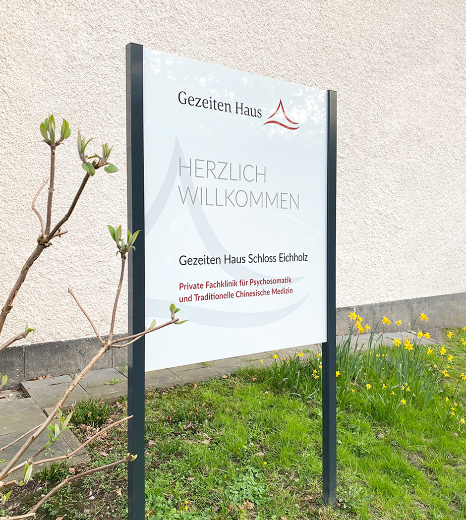 Willkommenstafel des Gezeiten Haus Schloss Eichholz, einer privaten Fachklinik für Psychosomatik und Traditionelle Chinesische Medizin, umgeben von frühlingshaften Blumen.