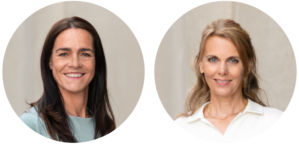 Porträt zweier Frauen mit lächelnden Gesichtern, die in professioneller Umgebung stehen. Beide tragen legere, elegante Kleidung und strahlen Freundlichkeit und Professionalität aus.