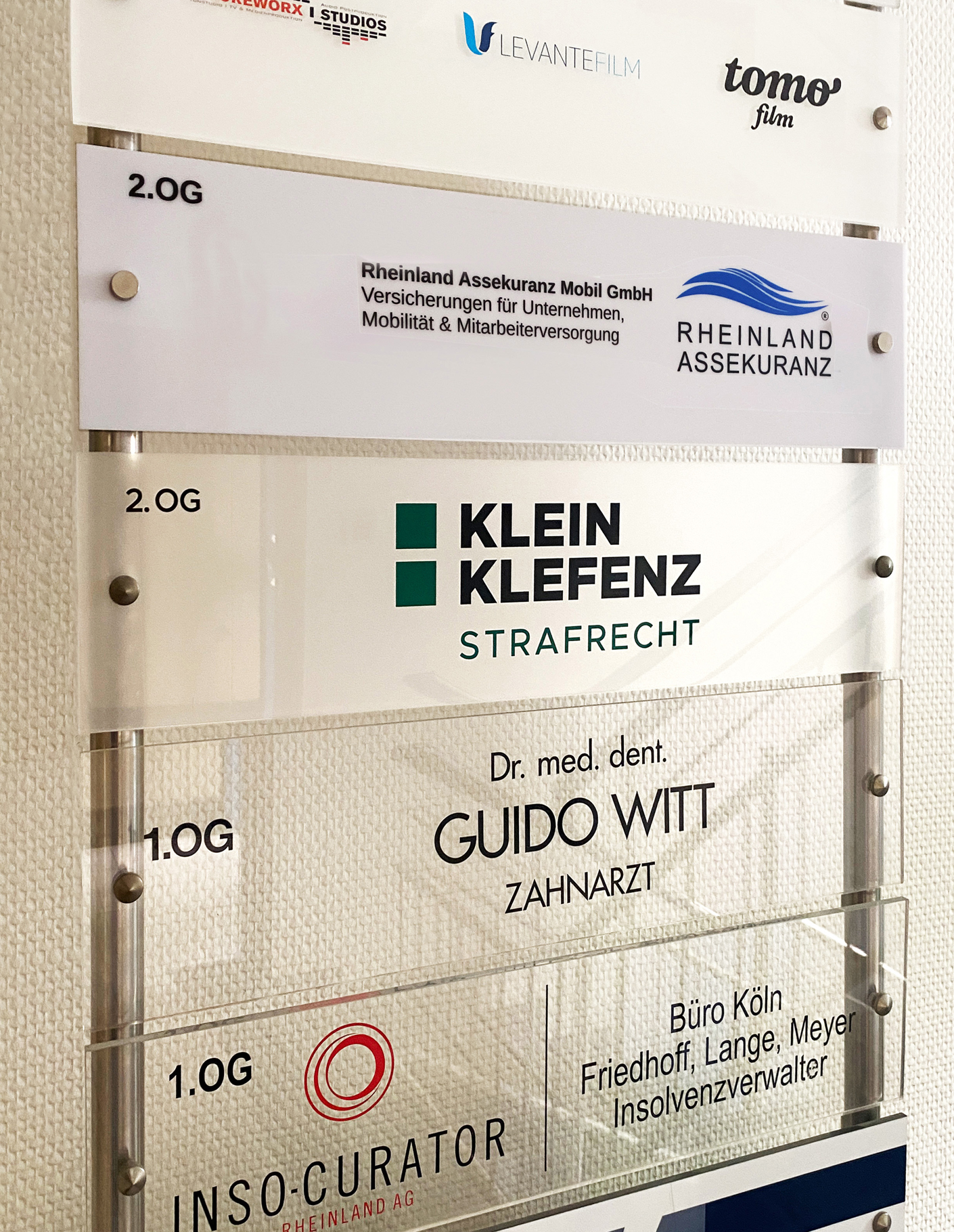 Schild mit Firmennamen und Dienstleistungen im 2. und 1. Obergeschoss, darunter Rheinland Assekuranz, Klein Klefenz Strafrecht, Dr. Guido Witt Zahnarzt und Insolvenzanwälte.